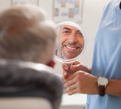 An older man admiring his new dental implant with a hand mirror