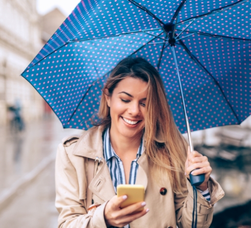 Smiling woman holding umbrella and looking at her phone